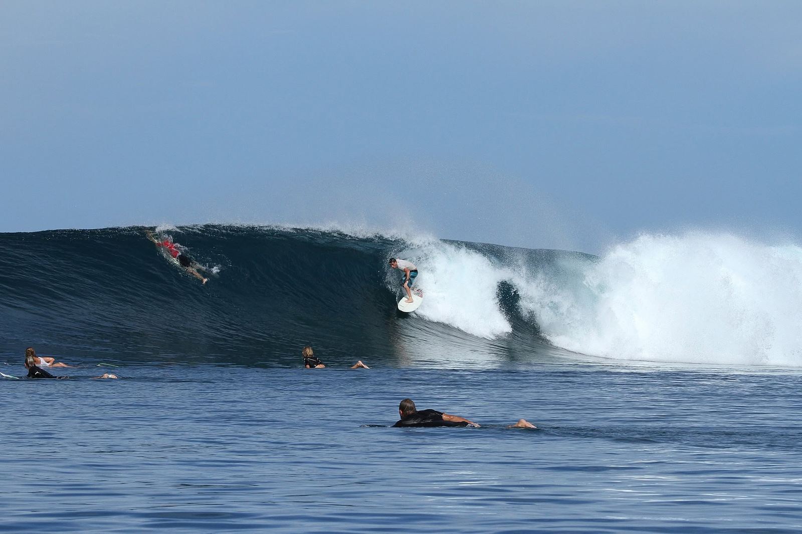 Kevin Perrow riding a heavy blue barrel while other surfers wait in the line-up